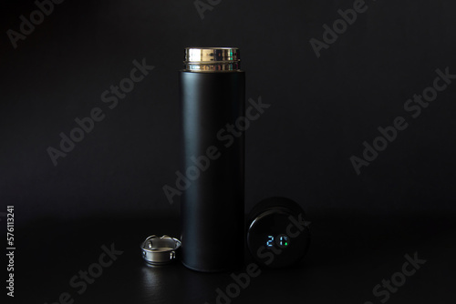 Black thermos with a strainer and a thermometer in the lid on a black background.