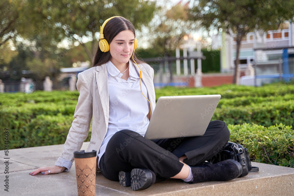 caucasian female college student using her laptop computer on the university campus with headphones on caucasian female college student using her laptop computer on the university campus with headphones on