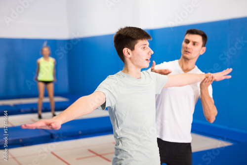 Male instructor helping teenage boy warming up before trampoline training in fitness center