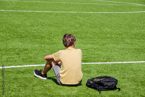 Foto Tired sad alone teenage boy with backpack sitting in empty sport stadium outdoors