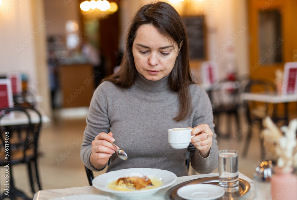 Woman enjoying fragrant espresso and slice of traditional apple strudel with vanilla sauce in coffee house while traveling in Vienna