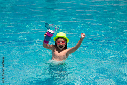 Child splashing in swimming pool. Active healthy lifestyle, swim water sport activity on summer vacation with child. Child hold cocktail. Fashion summer kid boy in hat and sunglasses.