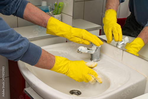 Man's hands in yellow gloves wiping the sink in the bathroom.