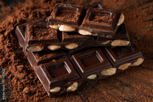Dark and milk chocolate with nuts on a dark background sprinkled with cocoa powder. © Vasiliy