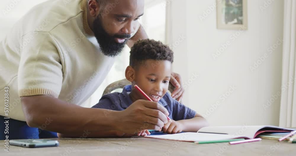 Happy african american father and son sitting at table and doing homework together, in slow motion Happy african american father and son sitting at table and doing homework together, in slow motion