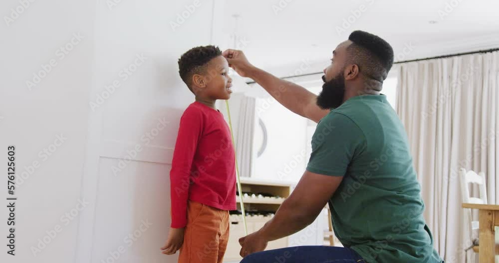 Happy african american father and son measuring height, in slow motion Happy african american father and son measuring height, in slow motion