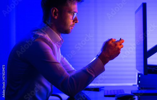 Man Browsing His Smartphone Apps in Front of Desktop Computer