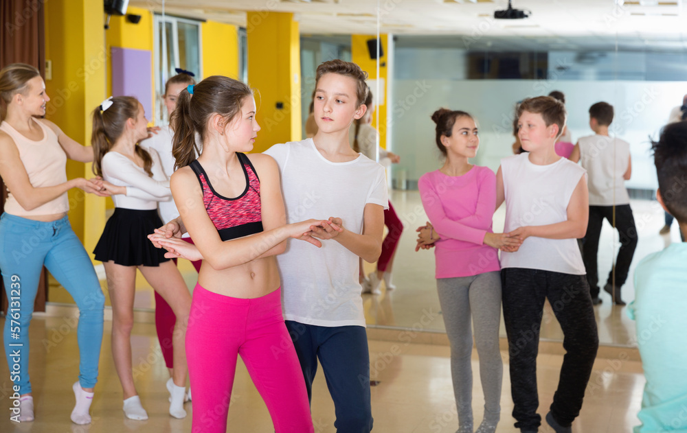 Cheerful positive children dancing rock-and-roll in pairs in choreography class with female trainer