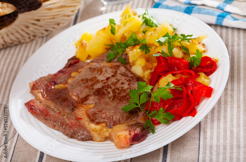 Juicy veal steak with vegetable garnish of fried potatoes, pickled bell pepper and fresh greens