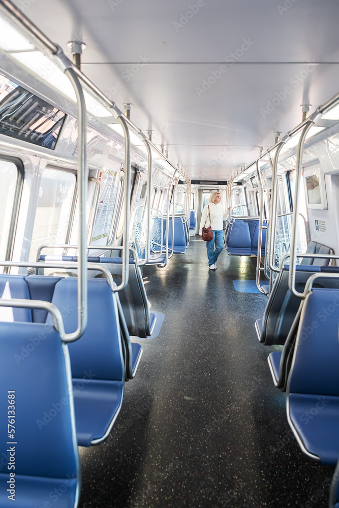 Blond-haired woman in an empty subway train in blue jeans while using public transport after a working day