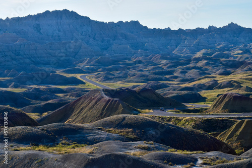 panorama of the mountains exposed rock strata with roadway cutting through blue sky and green grass plateaus badlands