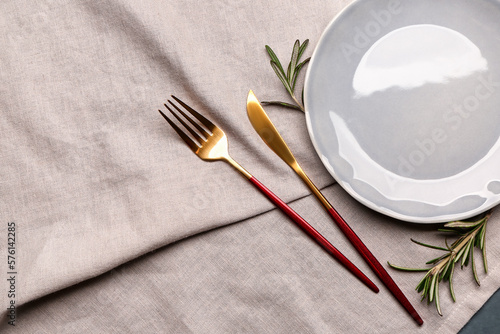 Fork, knife, plate and rosemary on grey tablecloth