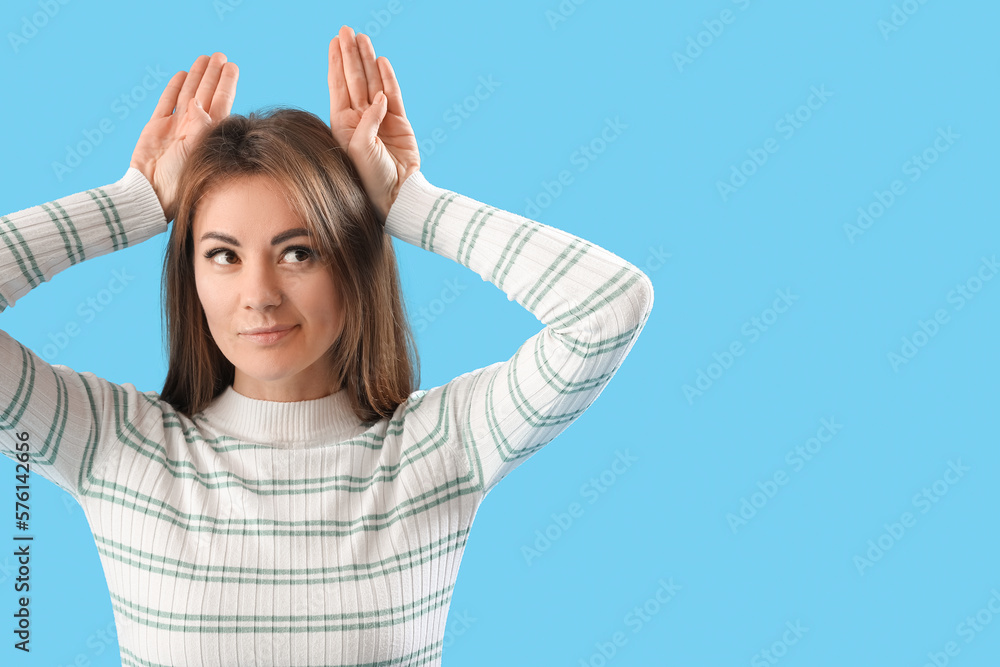 Beautiful woman making ears with her hands on blue background Beautiful woman making ears with her hands on blue background