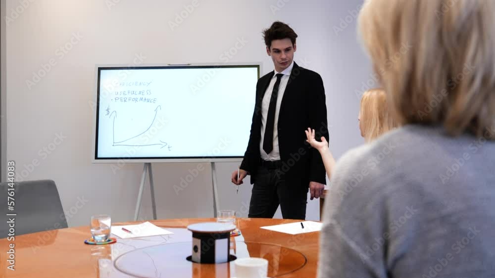 A young manager is discussing graphs on an interactive whiteboard at the workplace with his team. A young manager is discussing graphs on an interactive whiteboard at the workplace with his team.