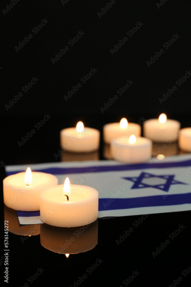 Burning candles with flag of Israel on dark background, closeup. International Holocaust Remembrance Day Burning candles with flag of Israel on dark background, closeup. International Holocaust Remembrance Day