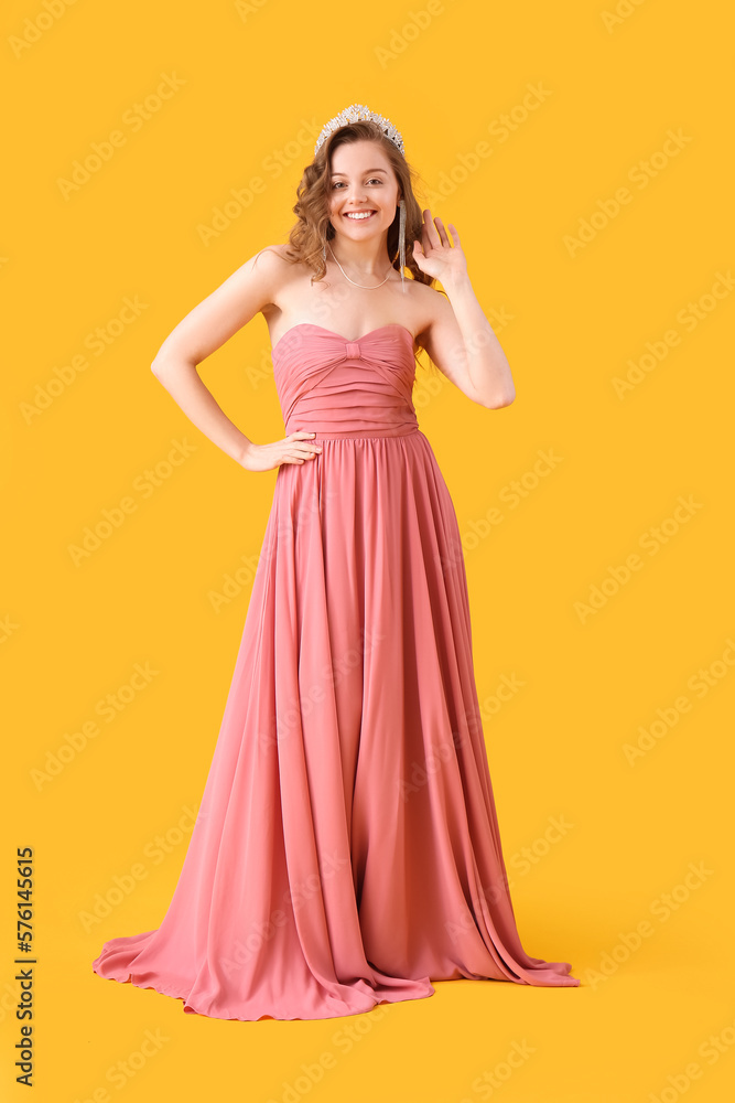 Young woman in tiara and prom dress on yellow background Young woman in tiara and prom dress on yellow background