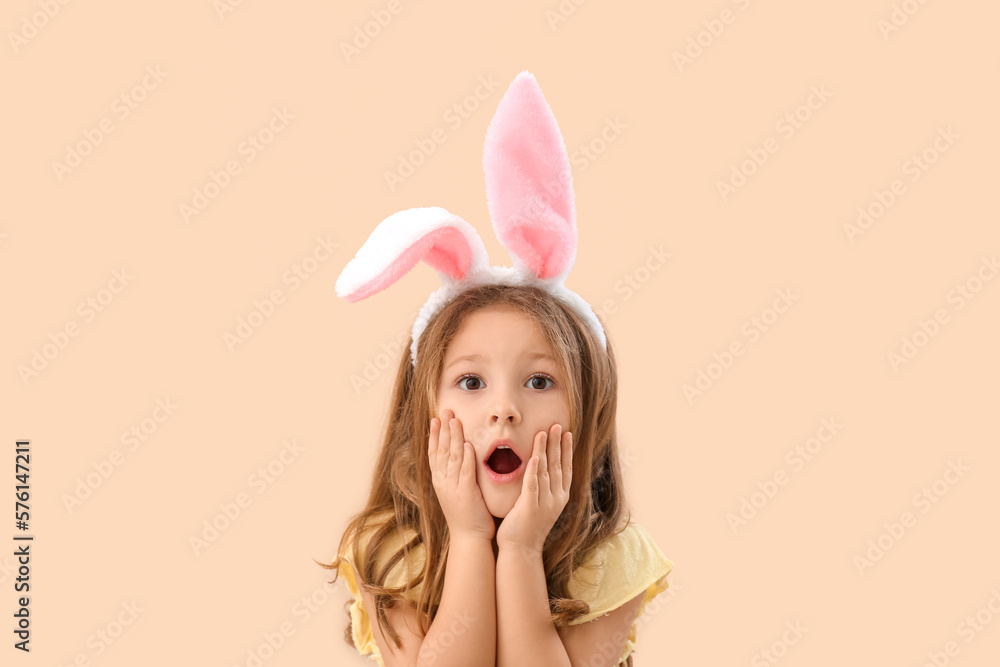 Shocked little girl in bunny ears on beige background
