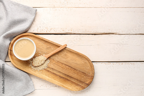 Board with bowl of tasty tahini and sesame seeds on light wooden background photo