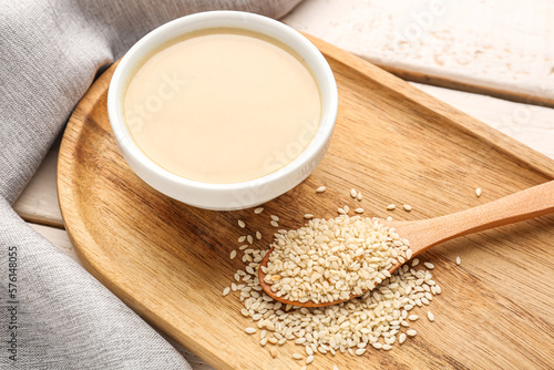 Board with bowl of tasty tahini and sesame seeds, closeup photo