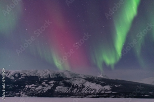 Incredible Aurora Borealis Northern Lights show seen in winter time over a frozen lake and snow capped mountains. 