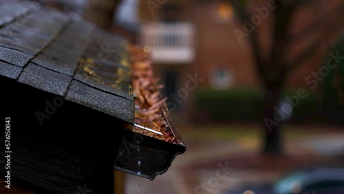 rain water rushing down the roof into the gutter clogged with fallen leaves