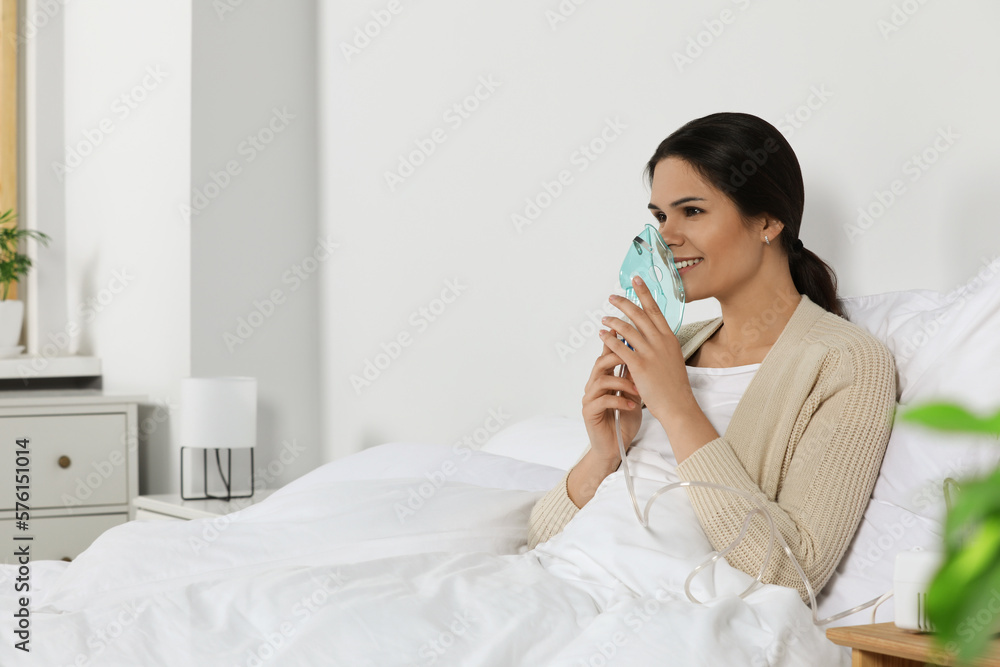 Young woman using nebulizer on bed at home, space for text Young woman using nebulizer on bed at home, space for text