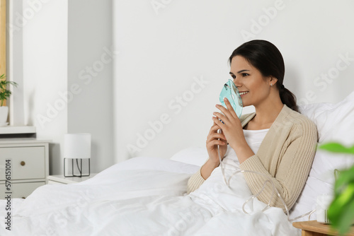 Young woman using nebulizer on bed at home, space for text