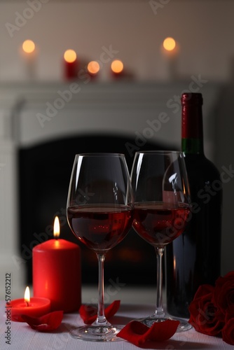 Glasses of red wine, burning candles and rose flowers on grey table indoors. Romantic atmosphere