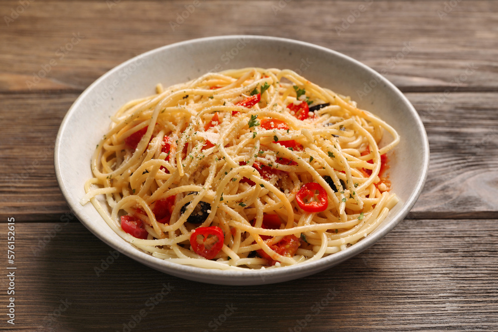 Bowl of delicious pasta with olives, tomatoes and parmesan cheese on wooden table