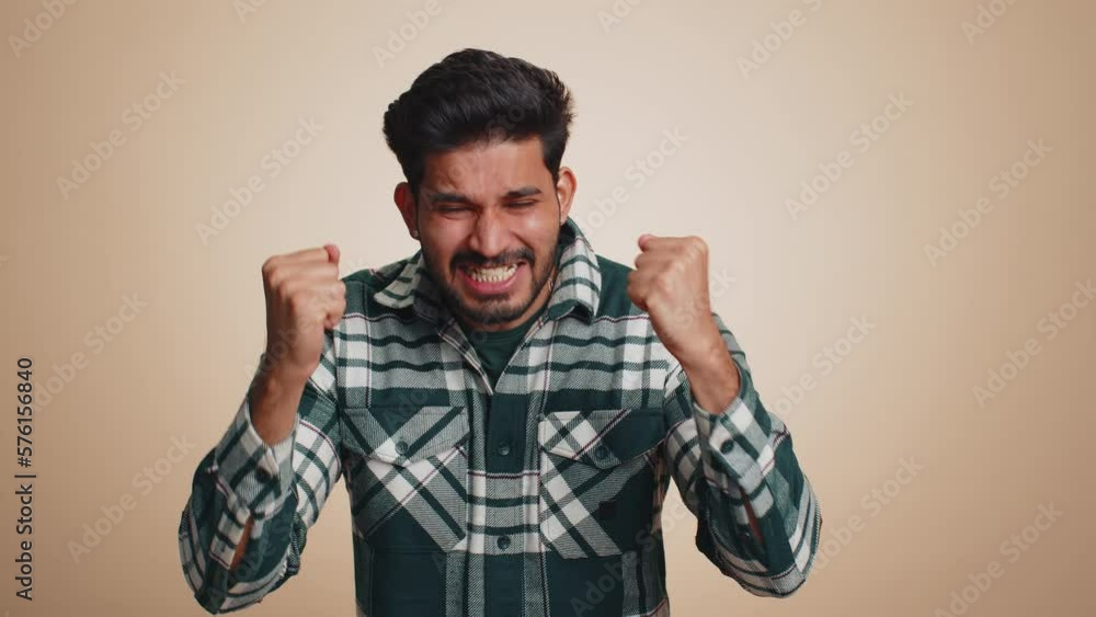 Indian man in shirt screams yell from stress tension problems feels horror hopelessness fear panic surprise shock expresses gestures rage. Handsome hindu guy isolated on beige studio background Indian man in shirt screams yell from stress tension problems feels horror hopelessness fear panic surprise shock expresses gestures rage. Handsome hindu guy isolated on beige studio background