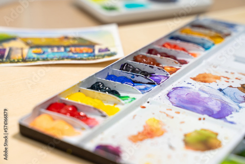 Colorful watercolor palette on table with watercolor set. Selective focus.
