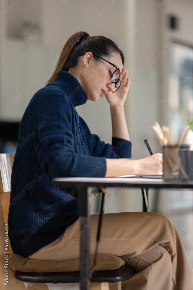 Asian women sitting in an office With stress and eye strain Tired, portrait of sad unhappy tired frustrated disappointed lady suffering from migraine sitting at the table, Sick worker concept	