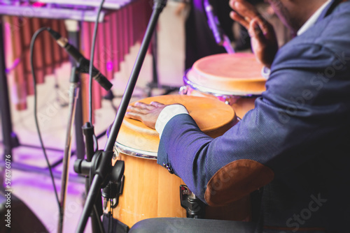 Bongo drummer percussionist performing on a stage with conga drums set kit during jazz rock show performance, tumbadora quinto with latin cuban afro-cuban jazz band performing in the background photo