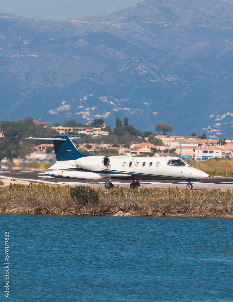 View of modern private reactive aircraft on an runway airfield ready to take off, airstrip with business jet airplane before the flight with mountains in the background in a summer sunny day View of modern private reactive aircraft on an runway airfield ready to take off, airstrip with business jet airplane before the flight with mountains in the background in a summer sunny day