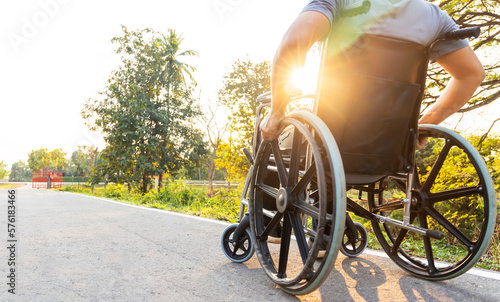 Disability man sitting on wheelchair in public park with sunray and light.His hand holding the wheel control.Selective focus at front wheel.Wheelchair for elderly with orthopedic problem.Copy space.
