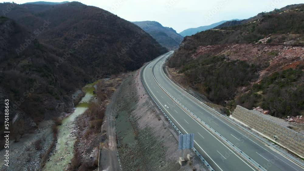 Scenic view of mountain road leading through river valley with cars driving, highway in Albania Scenic view of mountain road leading through river valley with cars driving, highway in Albania