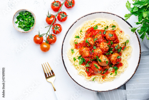 Spaghetti pasta with meatballs in spicy tomato sauce with parsley in plate, white table background, top view