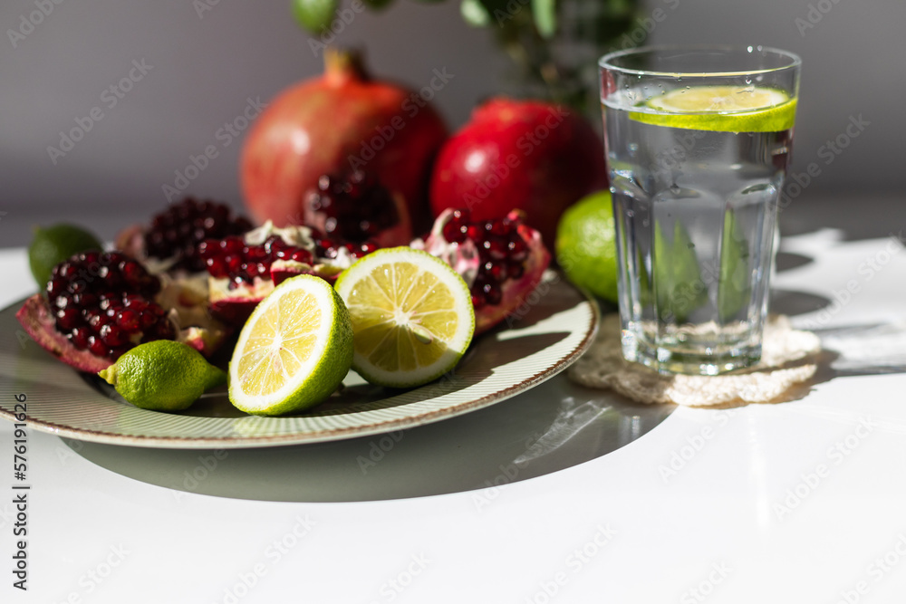 classic still life. ripe pomegranates and lime lie on a plate next to a vase with a red rose.. classic still life. ripe pomegranates and lime lie on a plate next to a vase with a red rose..