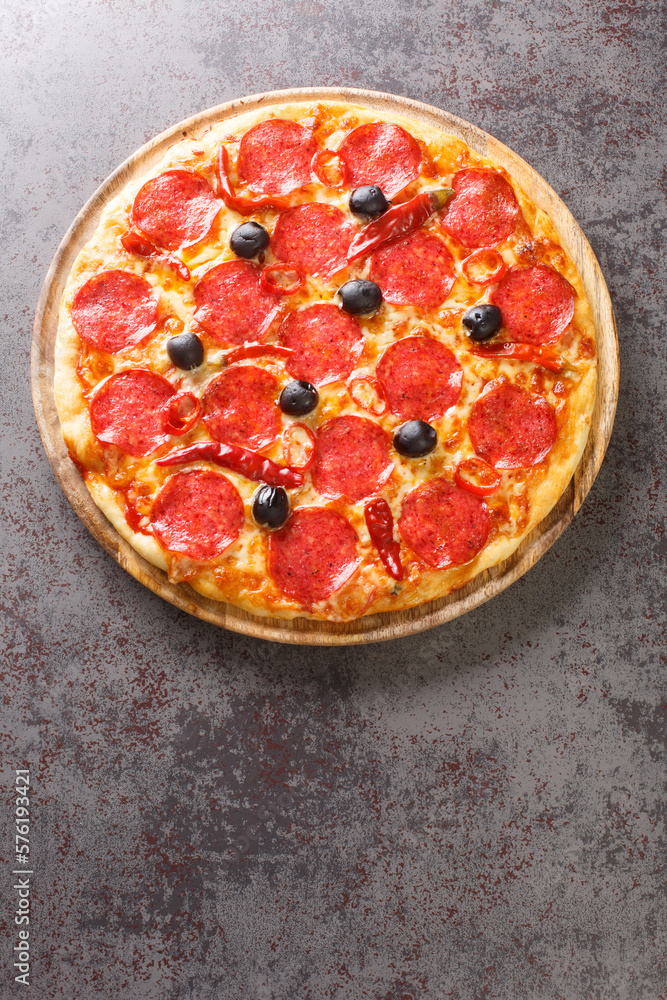 Spicy hot Diavola Pizza with sausage, mozzarella cheese, tomato sauce, chili peppers and black olives close-up on a wooden board on the table. Vertical top view from above Spicy hot Diavola Pizza with sausage, mozzarella cheese, tomato sauce, chili peppers and black olives close-up on a wooden board on the table. Vertical top view from above