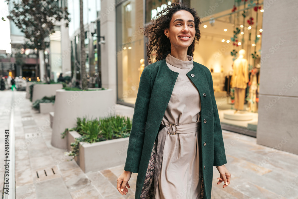 Fototapeta premium Portrait of young woman in green coat with curly hair in the city