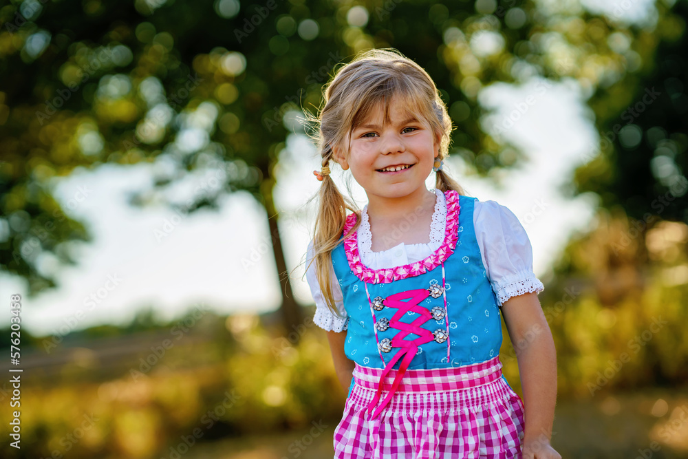 Cute little kid girl in traditional Bavarian costume in wheat field. Happy child with hay bale during Oktoberfest in Munich. Preschool girl play at hay bales during summer harvest time in Germany. Cute little kid girl in traditional Bavarian costume in wheat field. Happy child with hay bale during Oktoberfest in Munich. Preschool girl play at hay bales during summer harvest time in Germany.