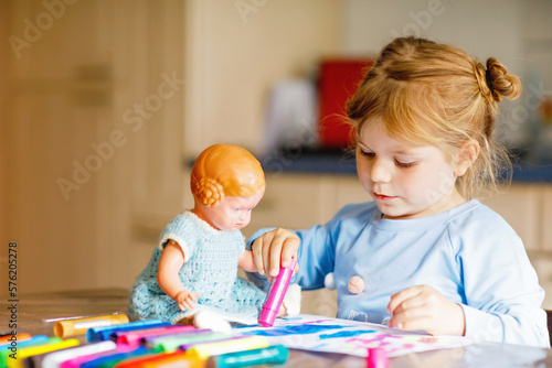 little alone toddler girl painting with felt pens during pandemic coronavirus quarantine disease. Happy creative child with old vintage doll, homeschooling and home daycare with parents