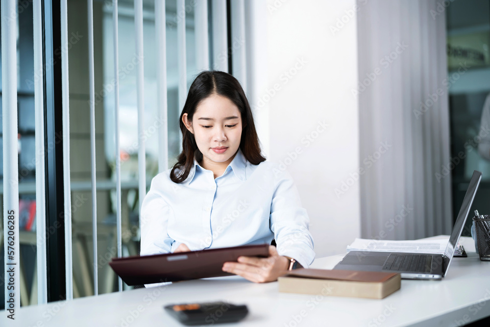Portrait of Asian Business woman working from office taking reading and writing notes in note pad working on laptop computer in her workstation Portrait of Asian Business woman working from office taking reading and writing notes in note pad working on laptop computer in her workstation