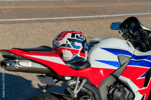 Motorcycle with red white and blue paint and helmet on seat with visible handle bars and exhaust pipe in view on street