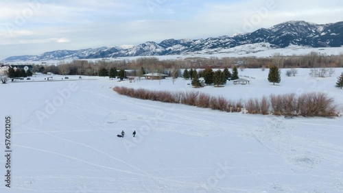 Boseman Montana Aerial Winter sunset ice fishermen pulling sled over snowy suburban park, orbit right with 4k drone with mountain backdrop at golden hour photo