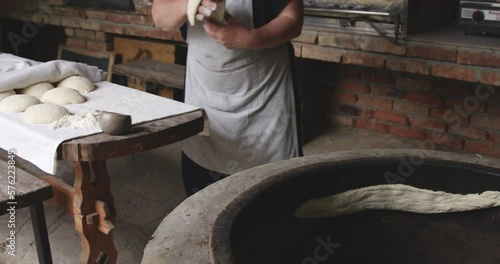 Woman in apron preparing by hand traditional shots puri flatbread in clay oven. photo