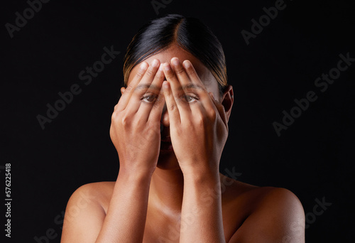 Hiding, shame and portrait of a woman covering face isolated on a black background in a studio. Shy, fear and girl with hands to cover eyes, an expression or insecurity about skin on a dark backdrop photo