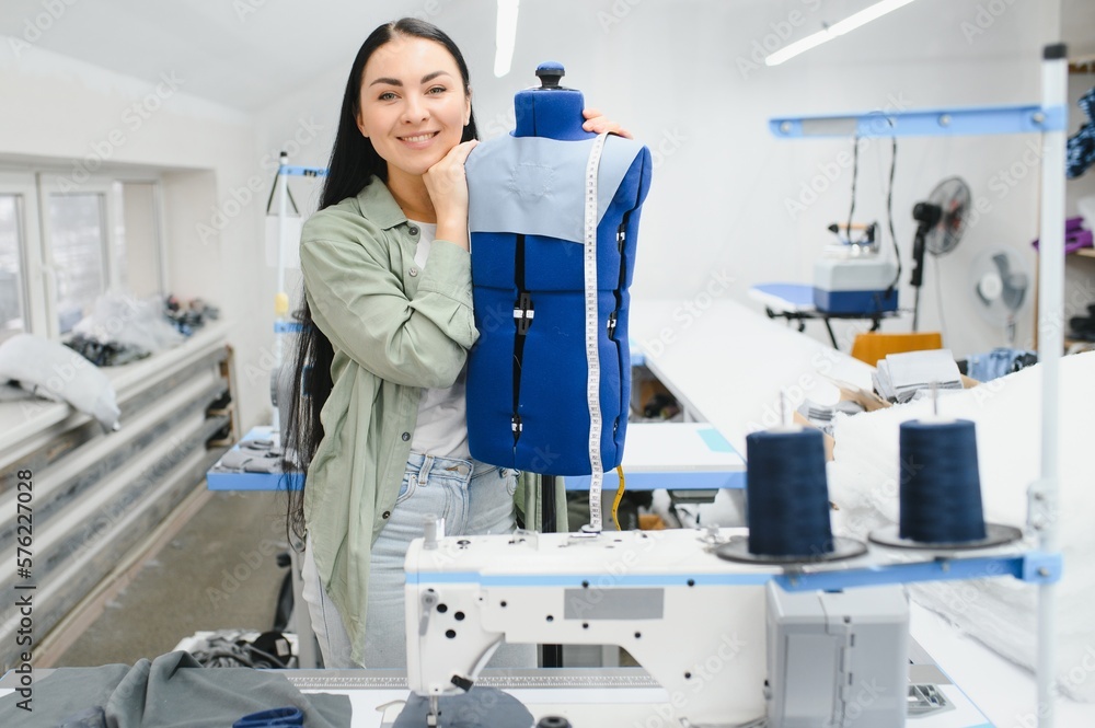 Fototapeta premium Happy female dressmaker working with sewing machine at textile factory.
