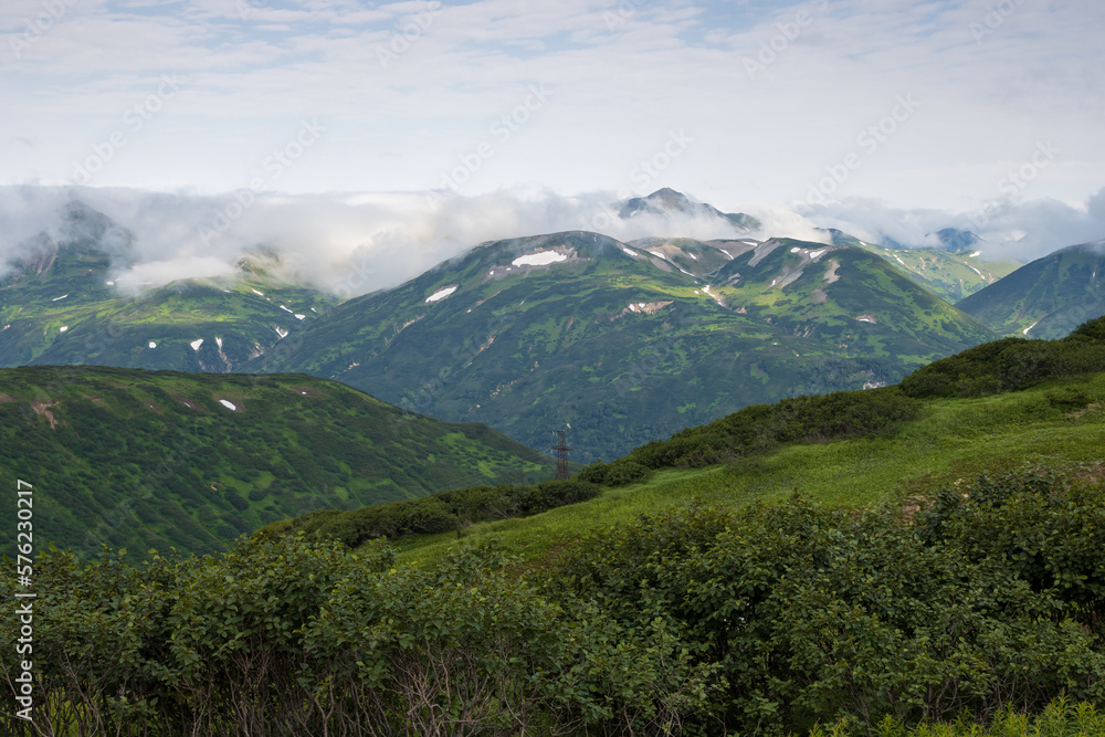 Summer mountain landscape. View of the mountain peaks. Low clouds. Travel, tourism and hiking on the Kamchatka Peninsula. Beautiful nature of Siberia and the Russian Far East. Kamchatka Krai, Russia.