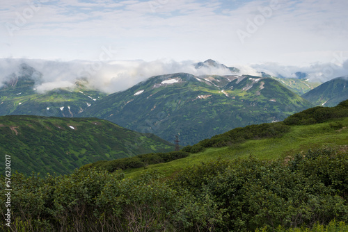 Summer mountain landscape. View of the mountain peaks. Low clouds. Travel, tourism and hiking on the Kamchatka Peninsula. Beautiful nature of Siberia and the Russian Far East. Kamchatka Krai, Russia.